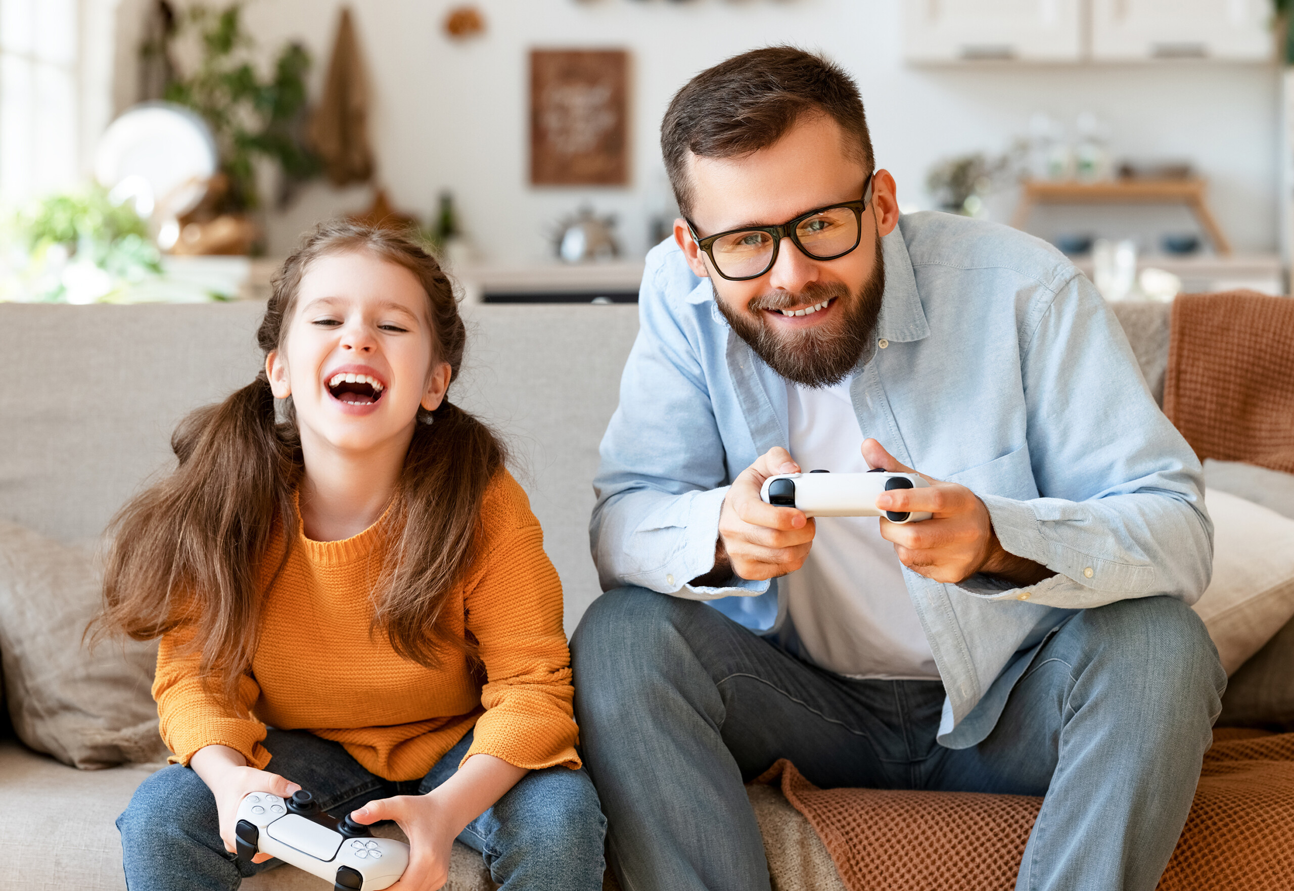 Vater und Tochter lachen und spielen gemeinsam Videospiele auf einer Spielkonsole