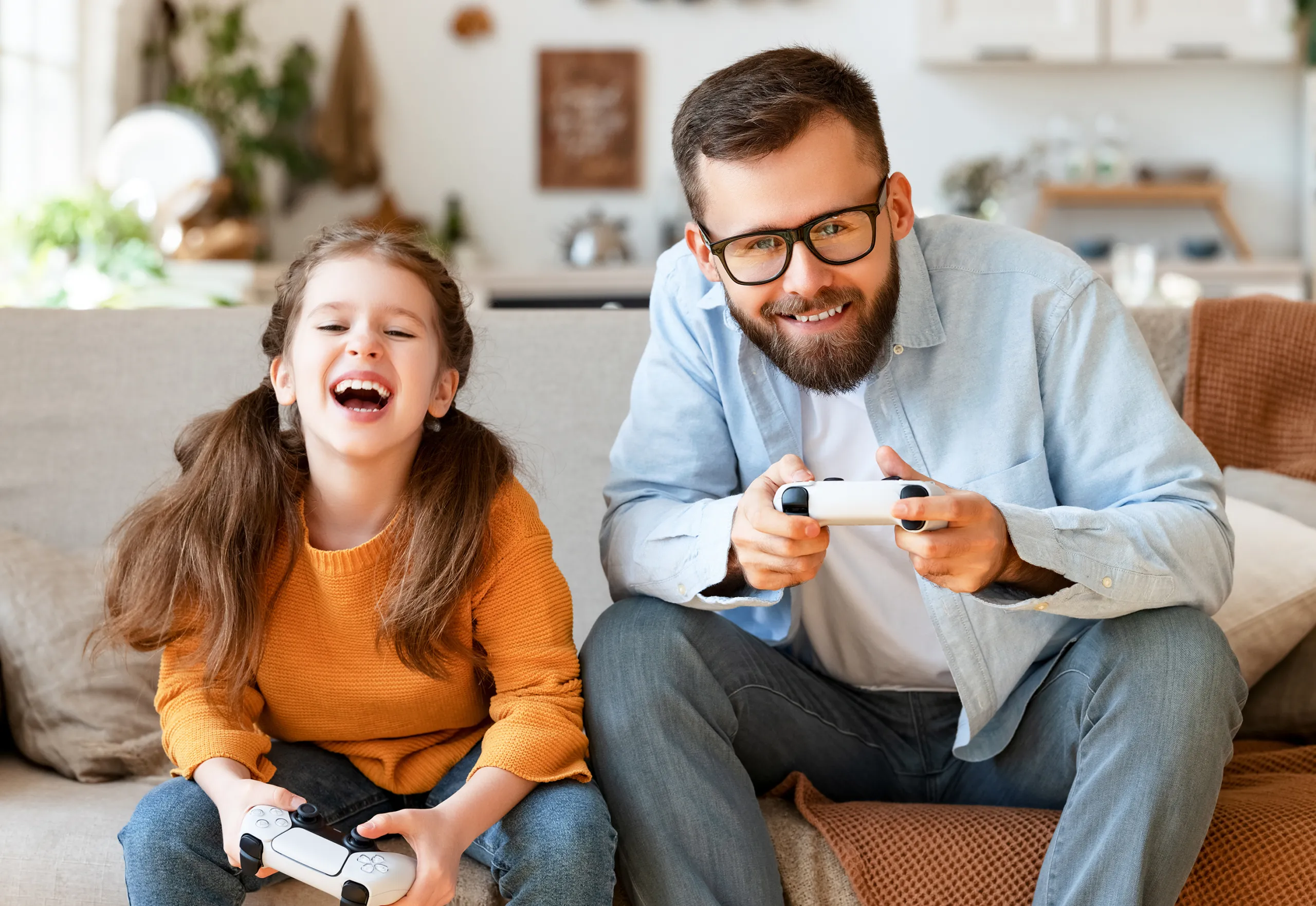 Vater und Tochter lachen und spielen gemeinsam Videospiele auf einer Spielkonsole